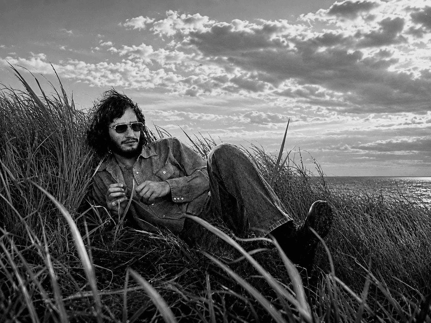 Arnie Jarmak reclining in beach grass beside the sea in Utila, Honduras, in 1974.