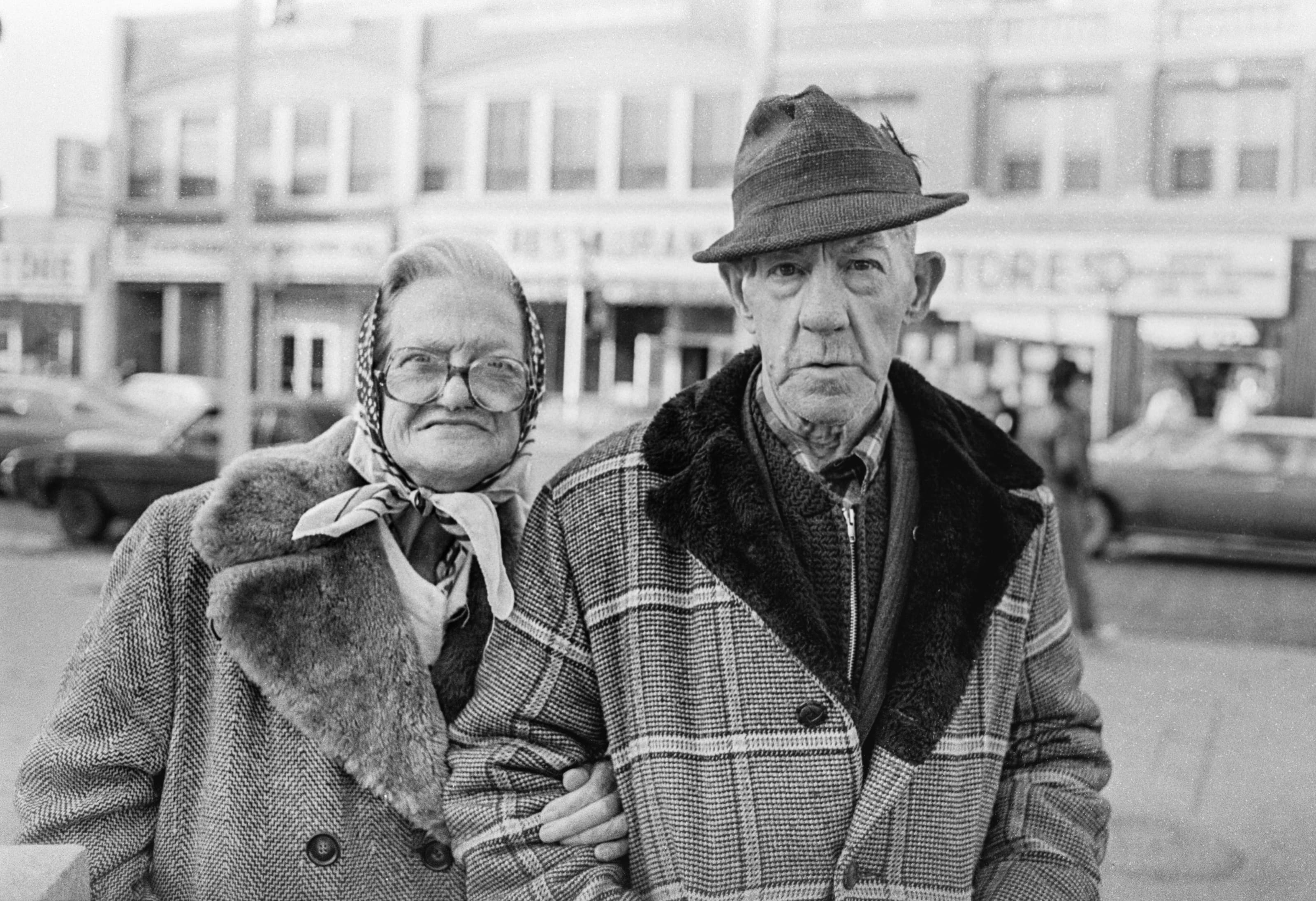 Black-and-white portrait of an older couple standing arm in arm on Broadway in Chelsea.