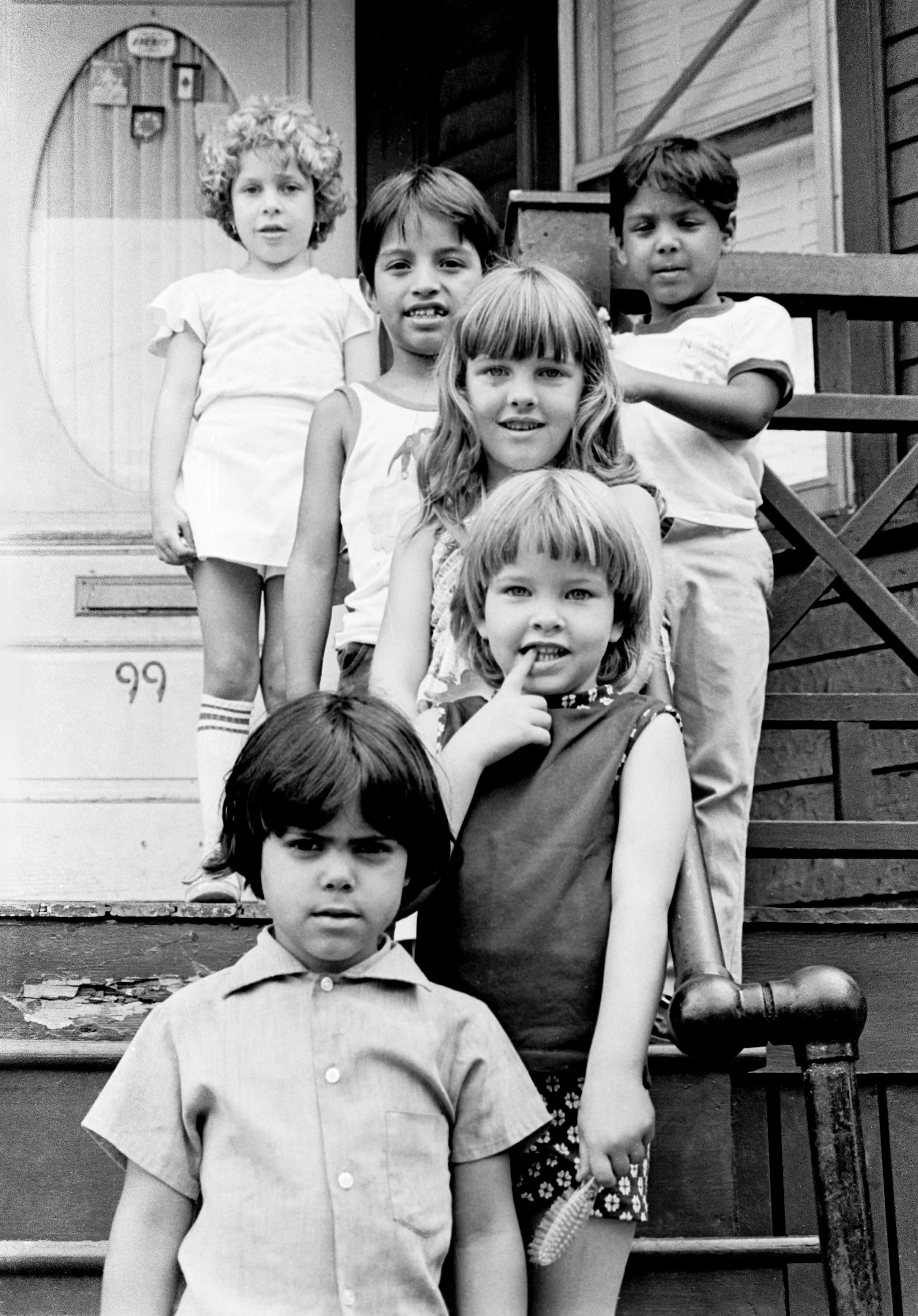 Black-and-white group portrait of six children gathered on the front steps of a Chelsea house marked number 99.