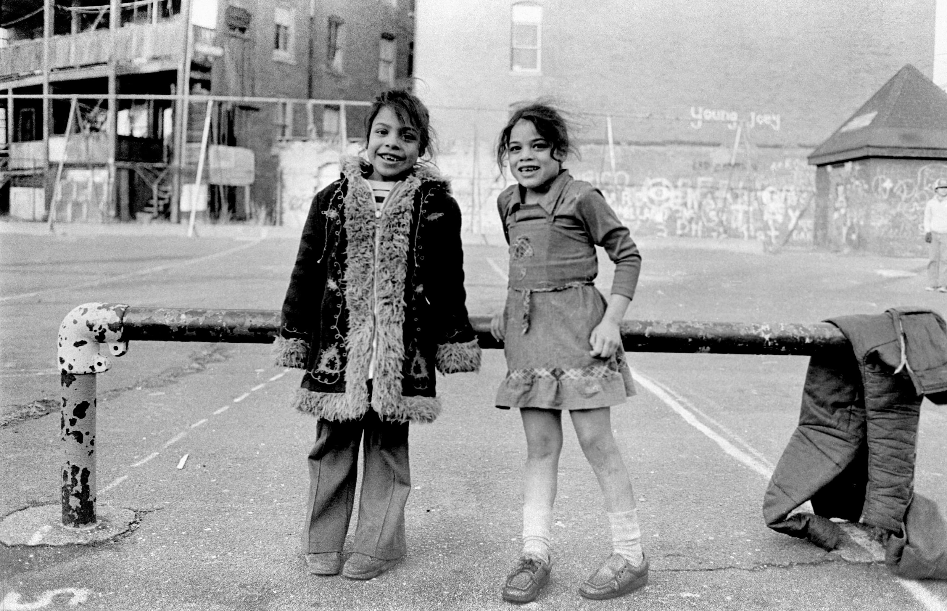 Black-and-white photograph of two girls standing beside a low rail in Polonia Park in Chelsea.