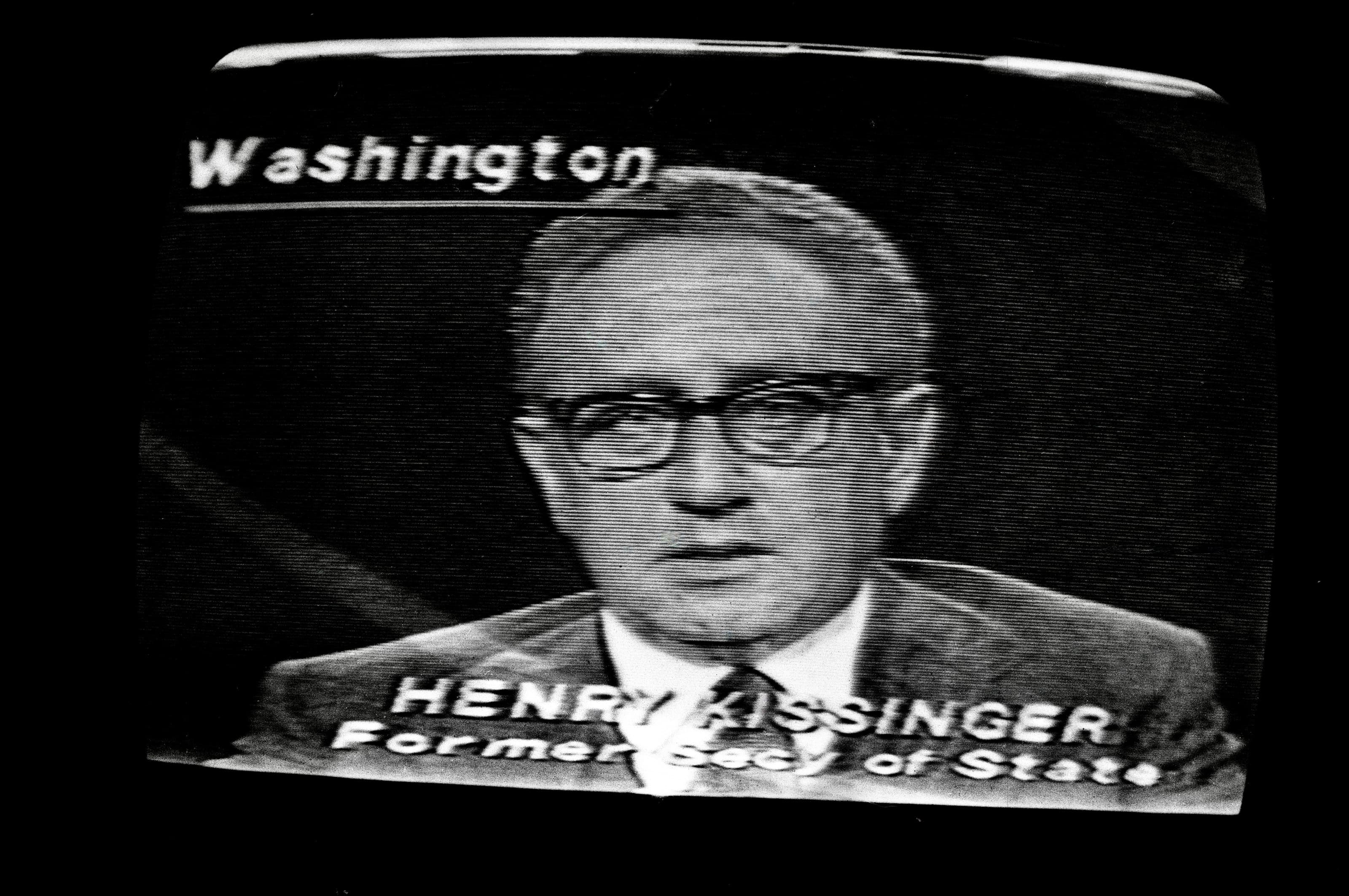Black-and-white photograph of a television screen showing Henry Kissinger on a Washington broadcast.
