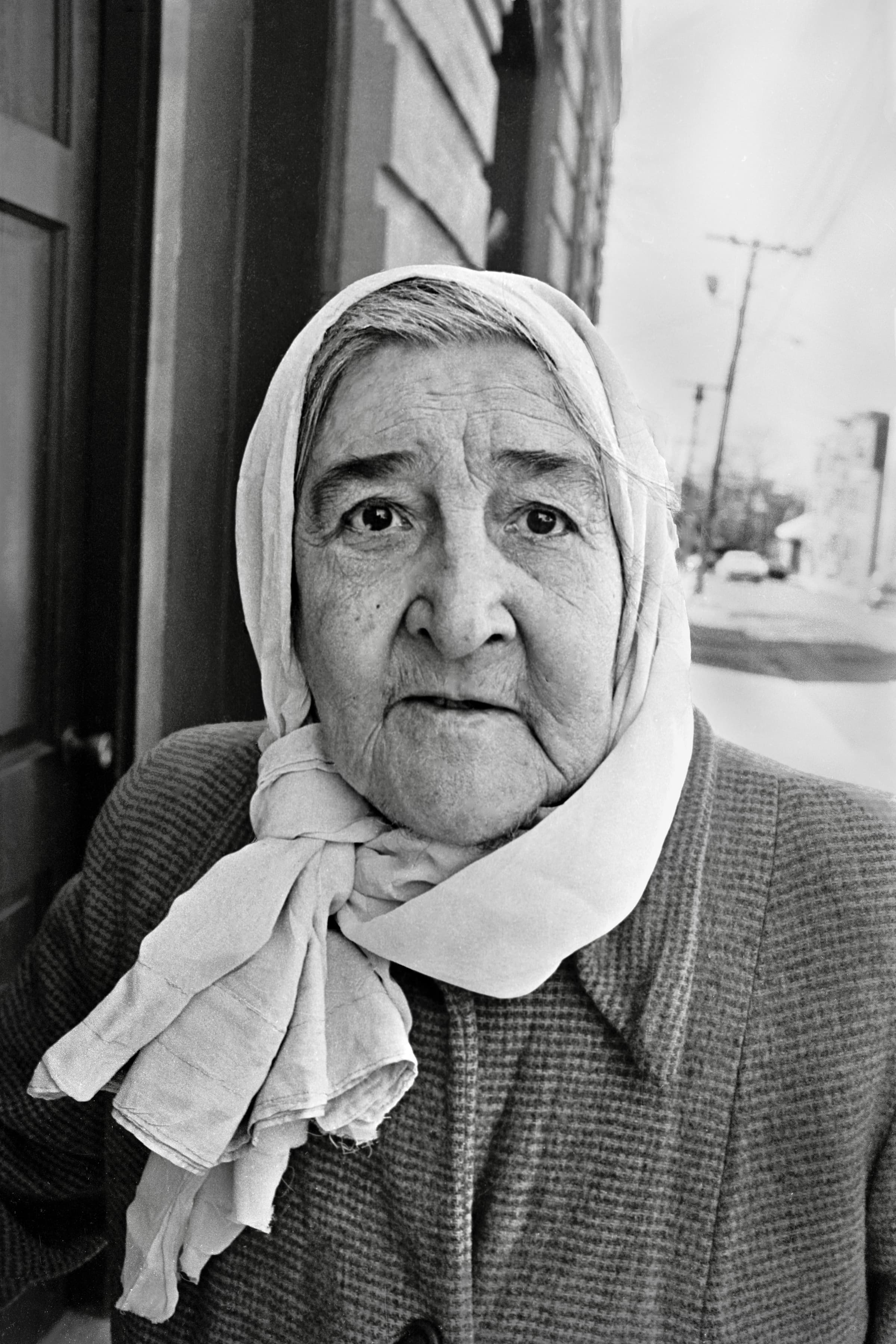 Black-and-white close portrait of an older woman wearing a kerchief.