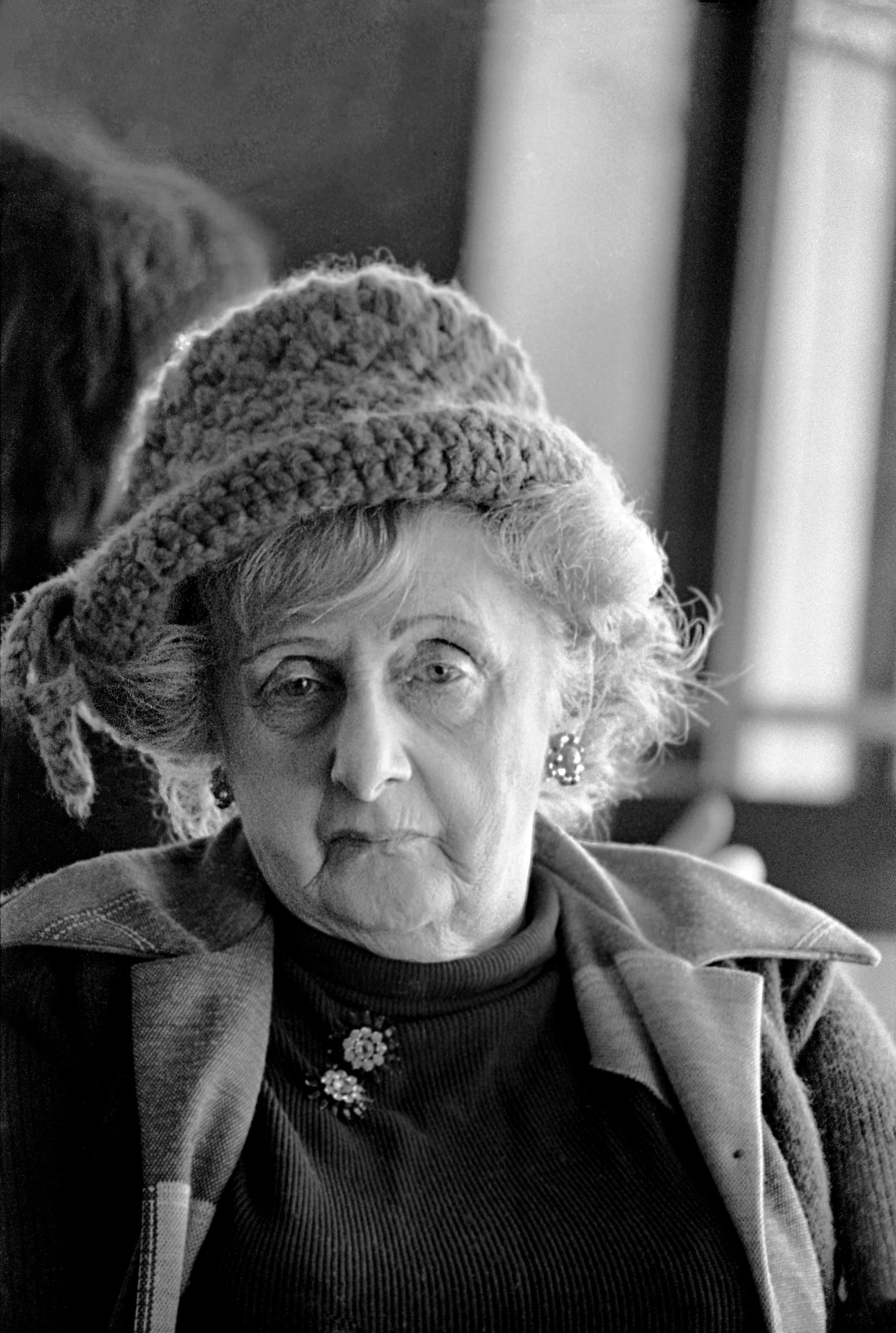Black-and-white portrait of an older woman wearing a knitted hat and coat.