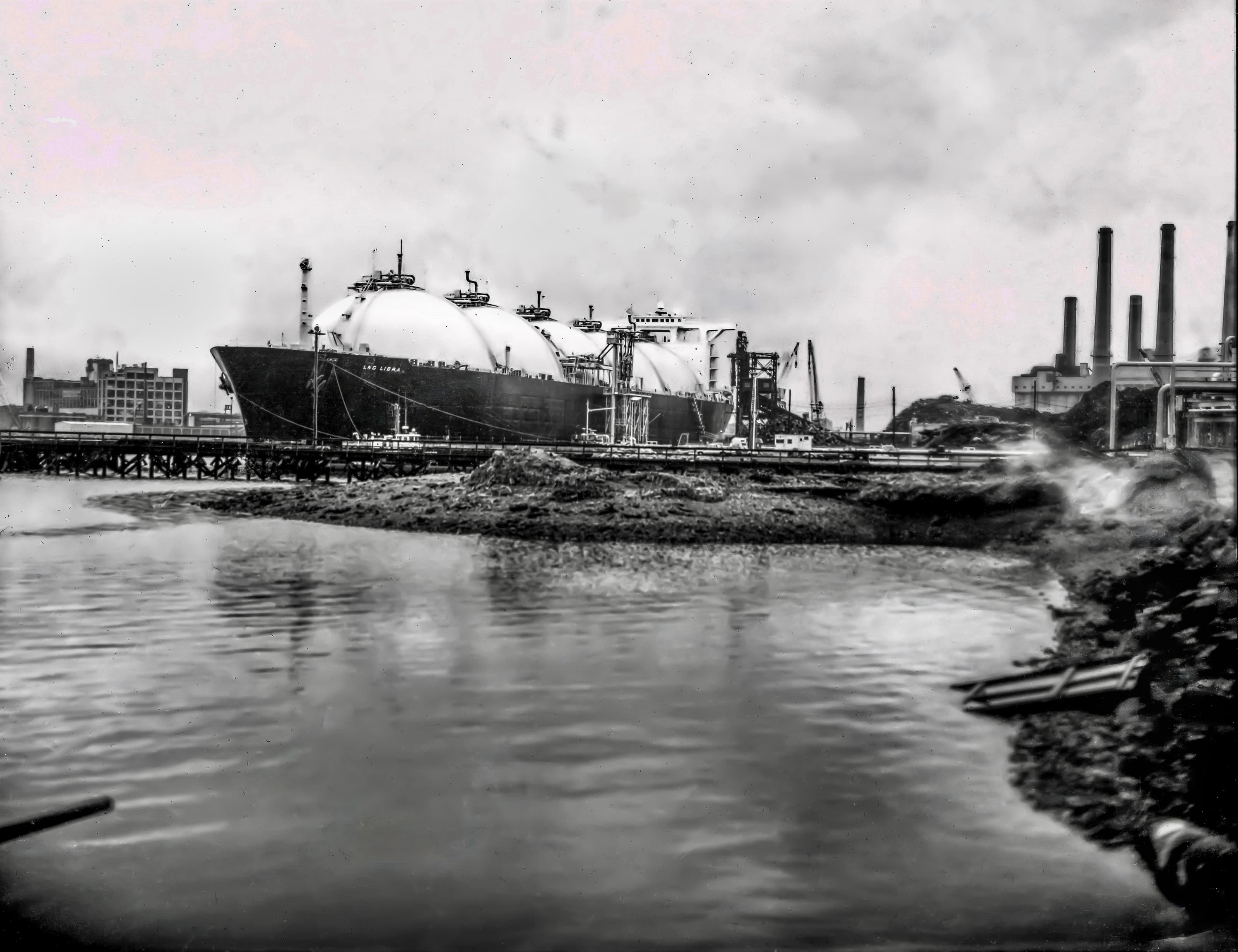 Black-and-white waterfront photograph of the LNG Libra unloading at an industrial terminal in Everett.