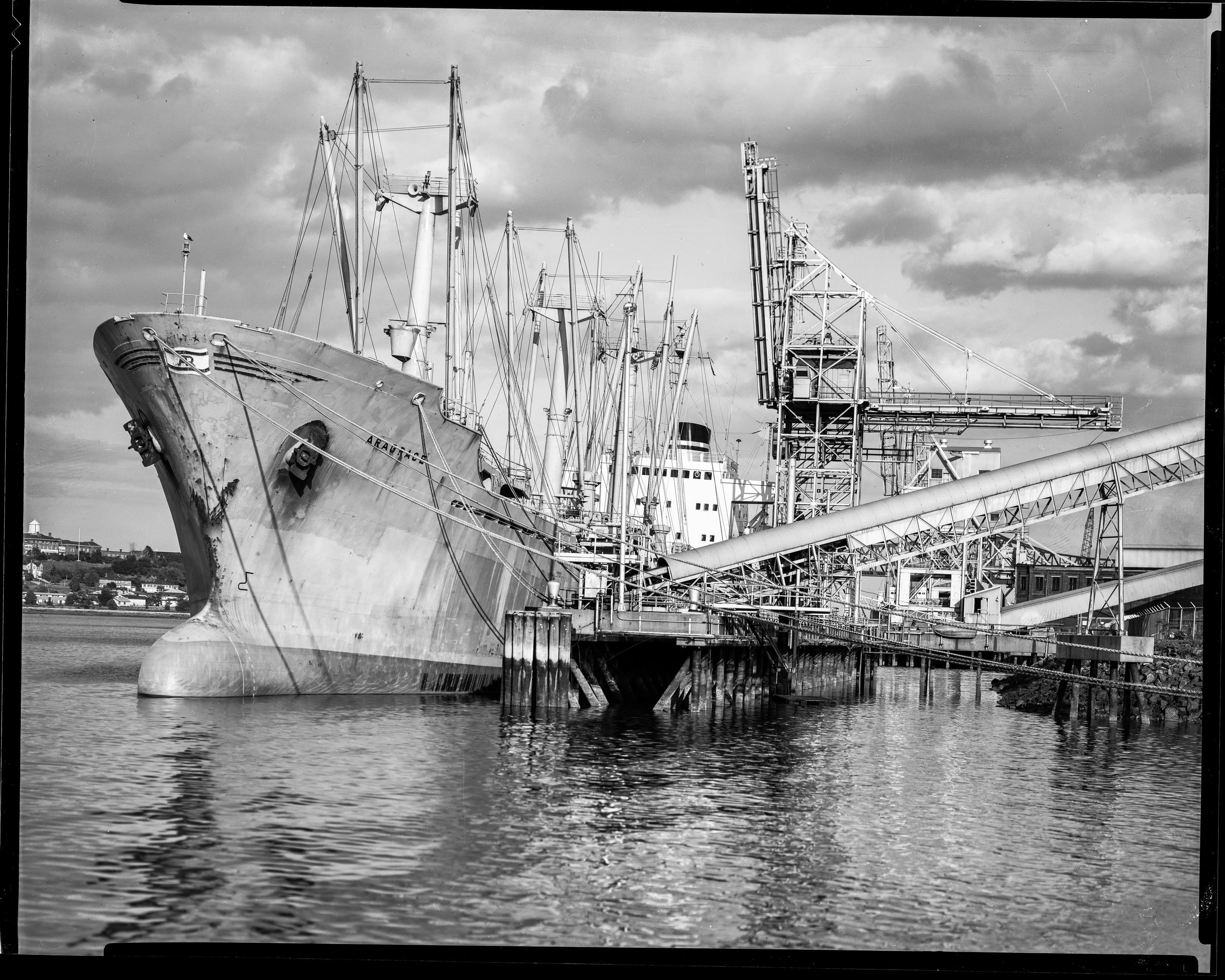 Black-and-white photograph of the cargo ship MV Aragrace at an industrial waterfront in Charlestown.