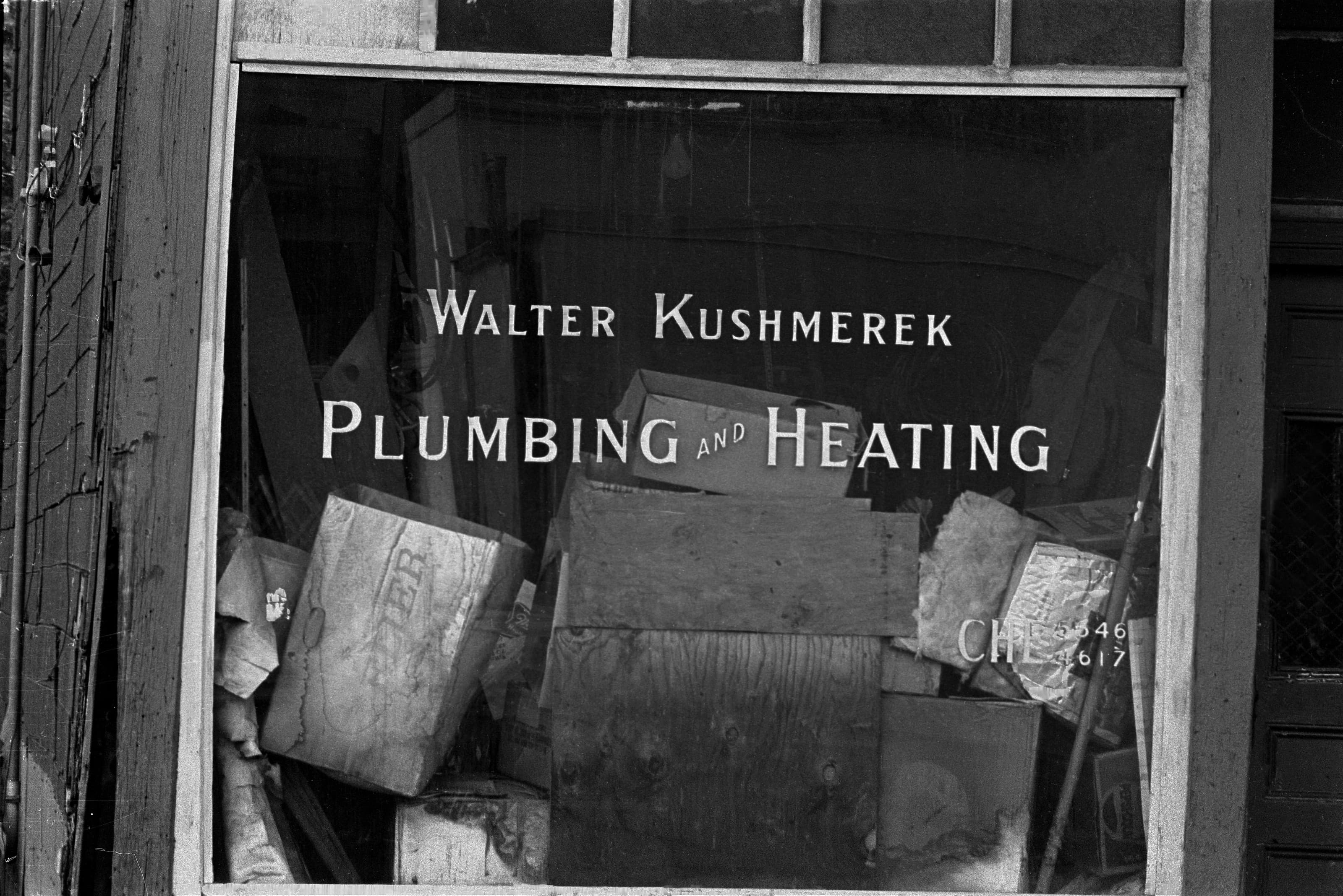 Black-and-white photograph of the Walter Kushmerek Plumbing and Heating storefront window.